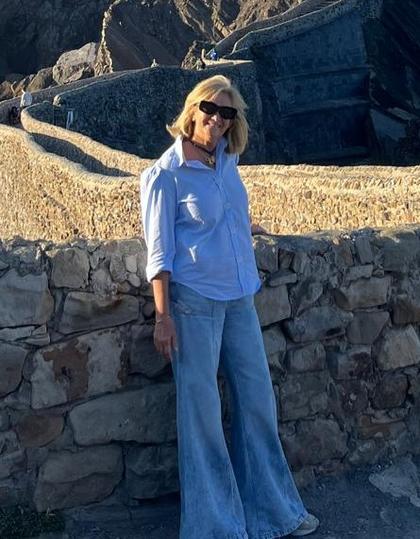 Una mujer con gafas de sol posa frente a un muro de piedra en un paisaje rocoso.