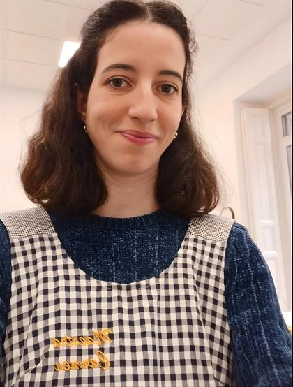 Una mujer sonriente con una blusa de cuadros y un suéter azul.