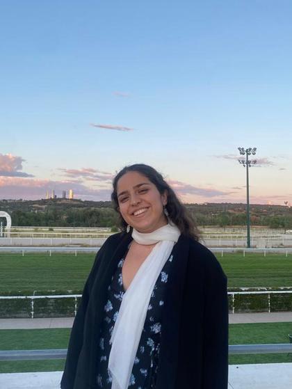 A smiling woman standing at a racetrack with the skyline in the background during sunset.