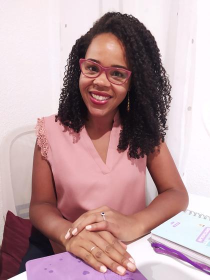 A smiling woman with curly hair wearing glasses and a pink blouse sitting at a table.