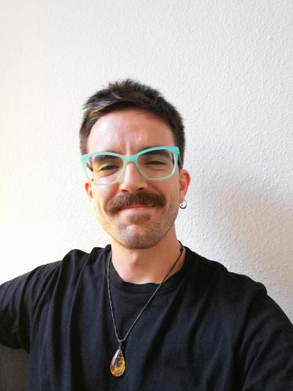 Hombre sonriendo con gafas de montura turquesa y camiseta negra.