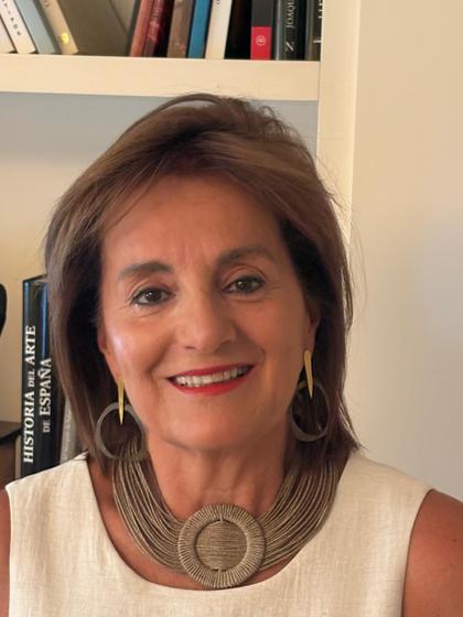 Una mujer sonriente con un collar grande, posando ante una estantería llena de libros.