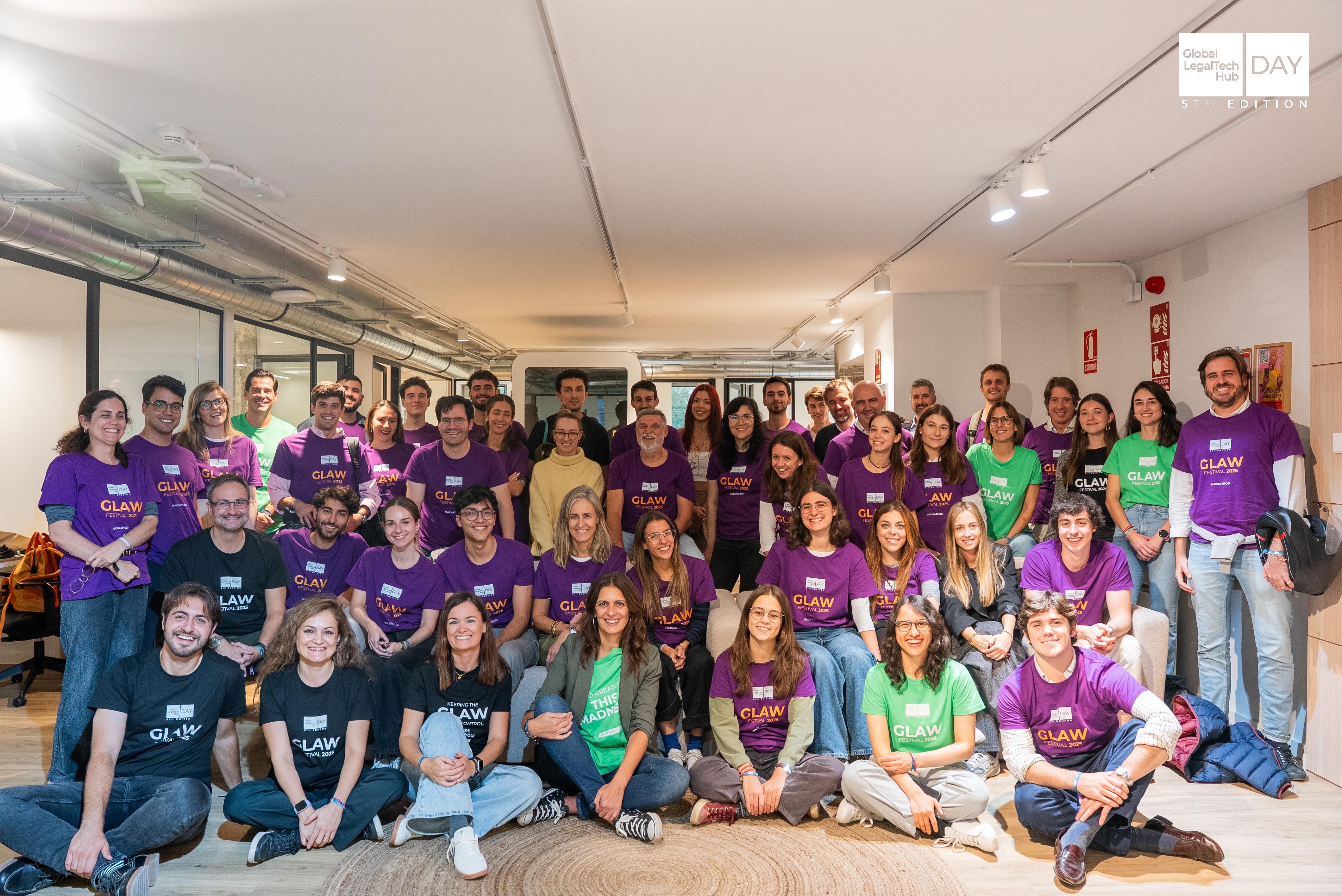 Un grupo grande de personas de pie en un espacio de oficina, vistiendo camisetas de diferentes colores.
