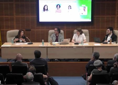 A panel discussion at a conference with four speakers and an audience in a lecture hall.