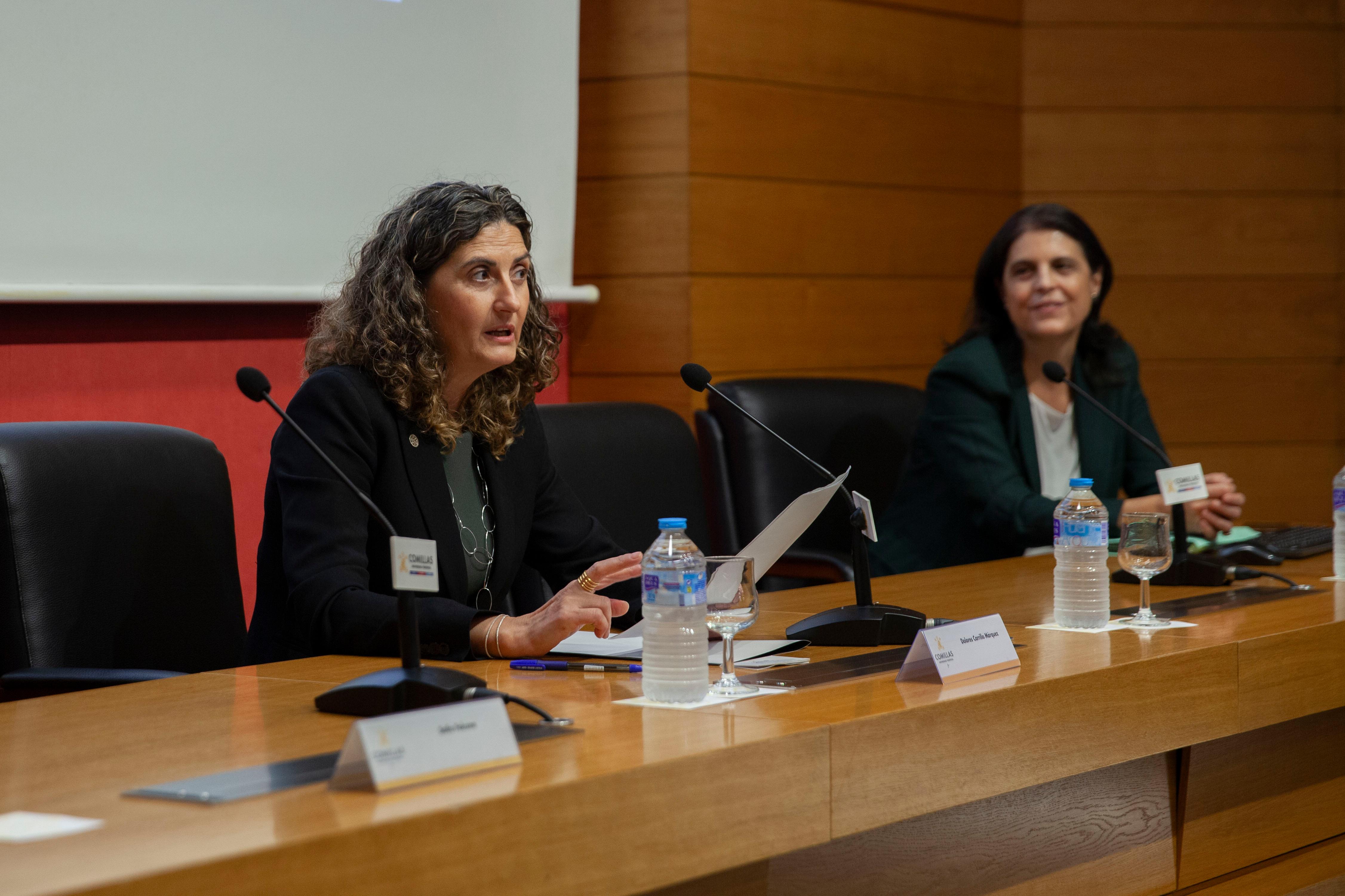Una mujer habla en una conferencia mientras otra la escucha desde el lado.