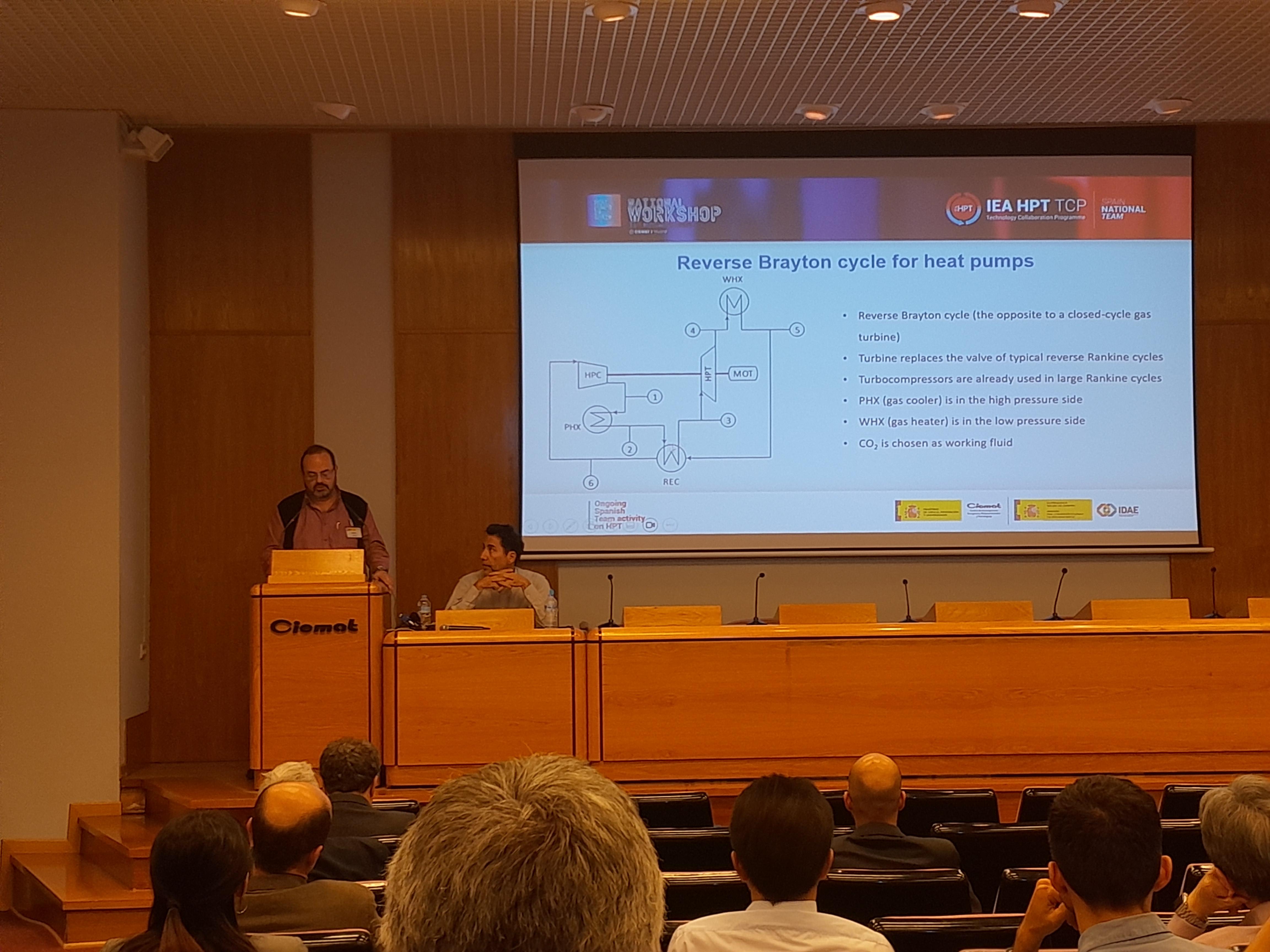 A person presenting a lecture on 'Reverse Brayton Cycle for Heat Pumps' in a conference room filled with attendees.