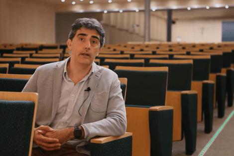 A man sitting in an empty lecture hall looking towards the camera.