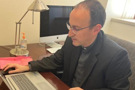 Un sacerdote utilizando una computadora portátil en un escritorio organizado.