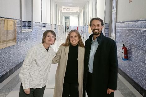 Tres personas sonriendo y posando para una foto en un pasillo con azulejos azules en las paredes.