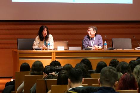 Una conferencia en un auditorio con dos ponentes en el escenario y un público atento.