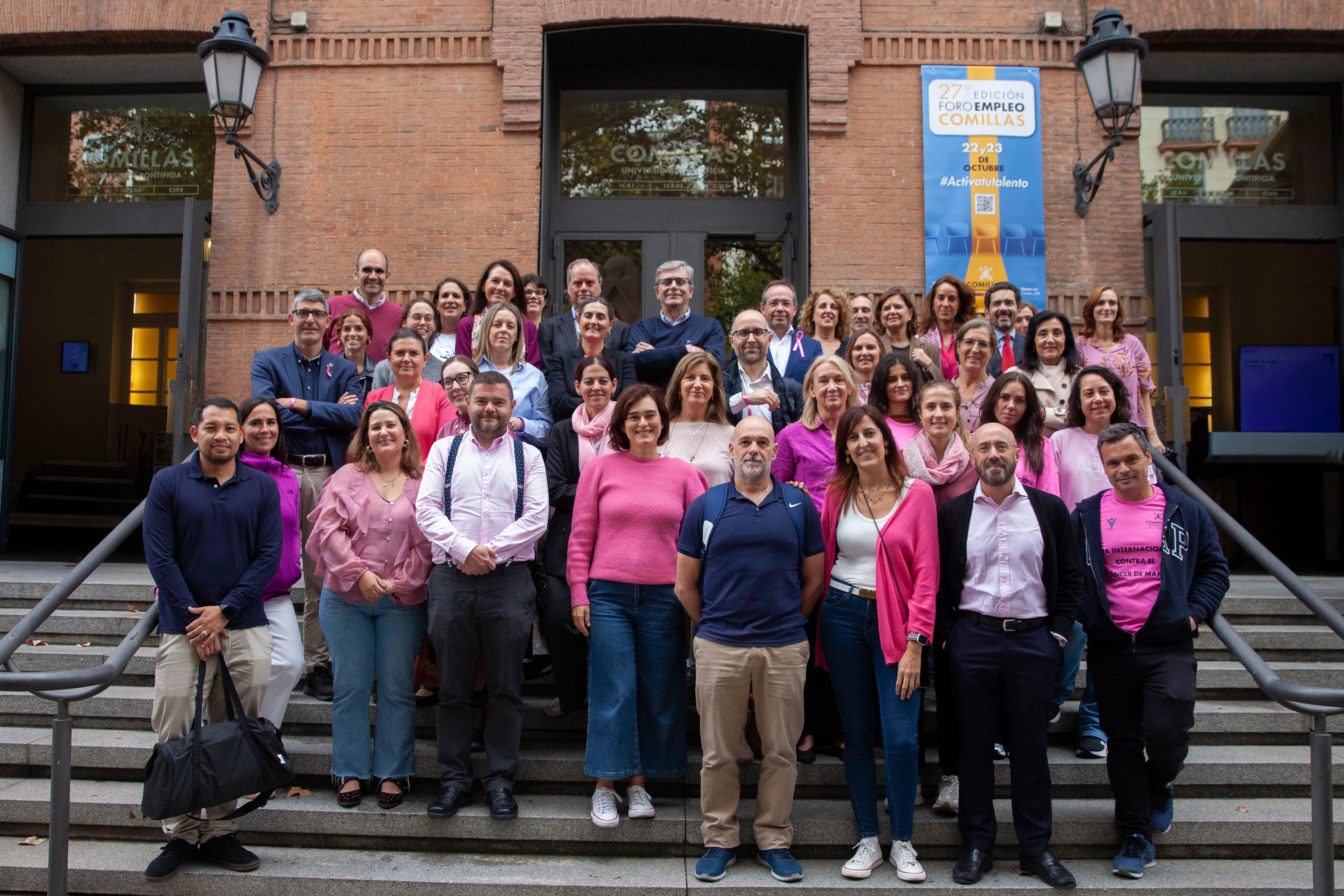 Un grupo de personas posando en escaleras frente a un edificio, vistiendo ropa de color rosa.