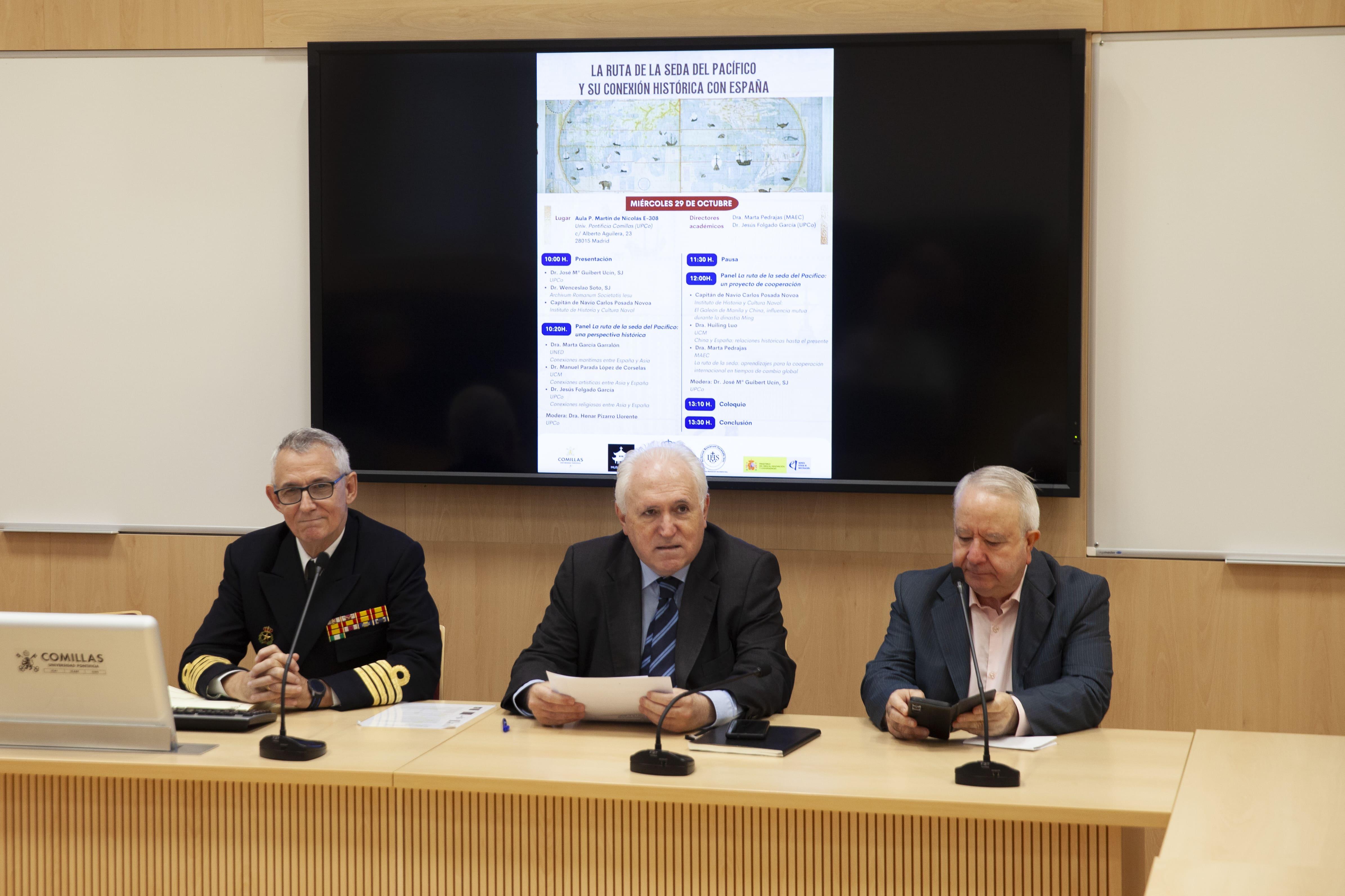 Tres hombres están sentados frente a una pantalla mostrando información en una sala de conferencias.