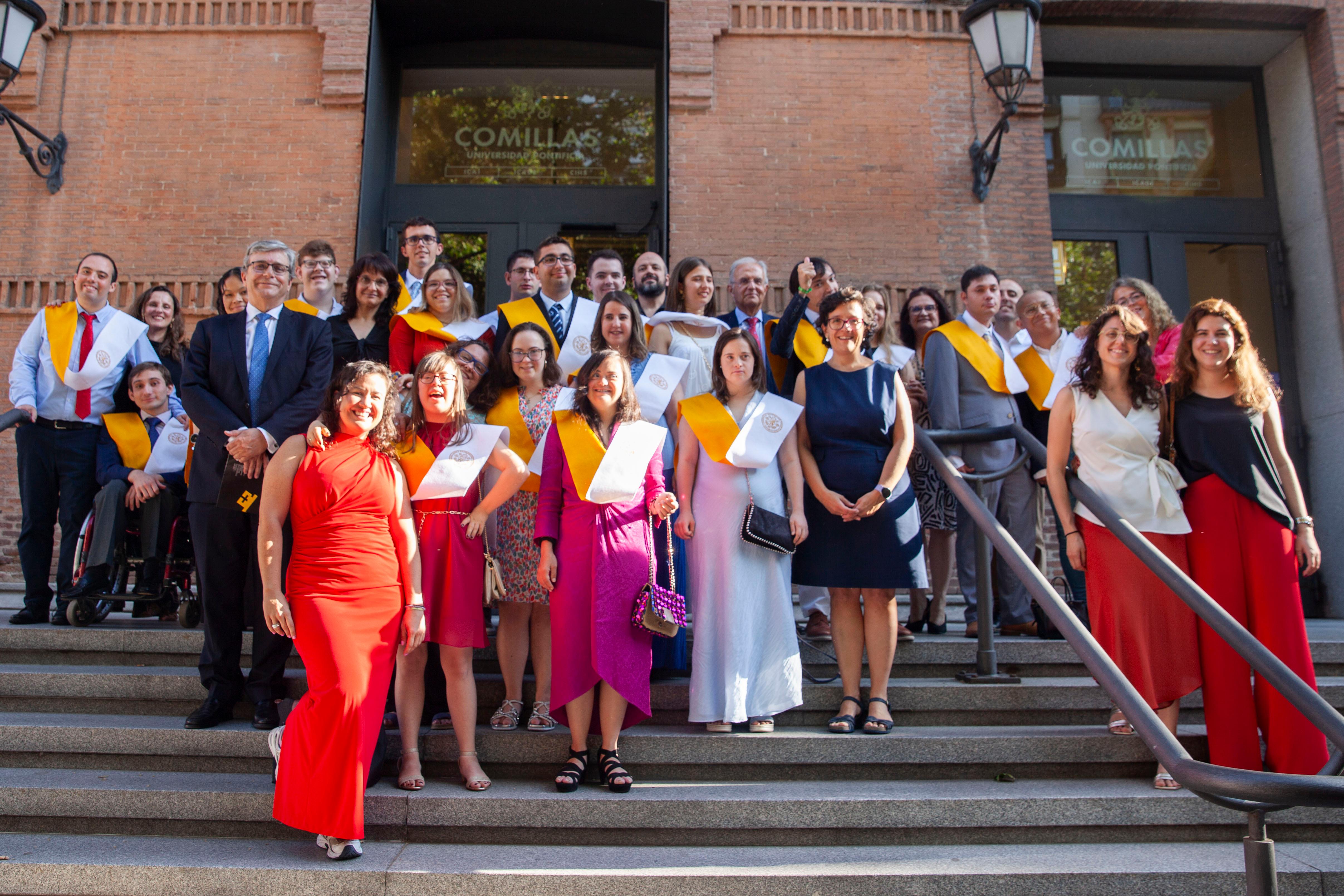 Grupo de graduados posando en la entrada de un edificio con togas y diplomas.