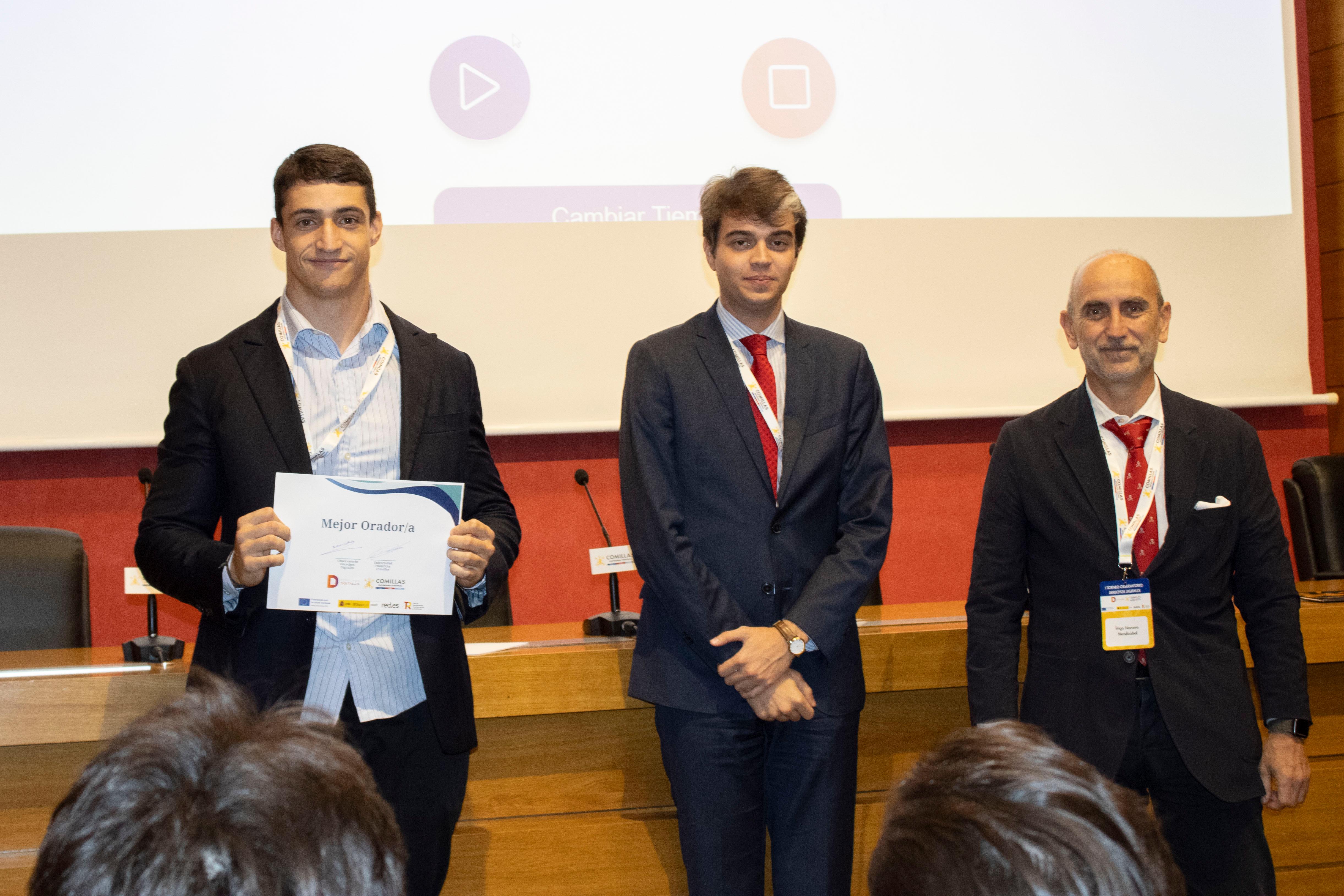 Tres hombres posan en un evento, uno de ellos sostiene un certificado destacando su logro.