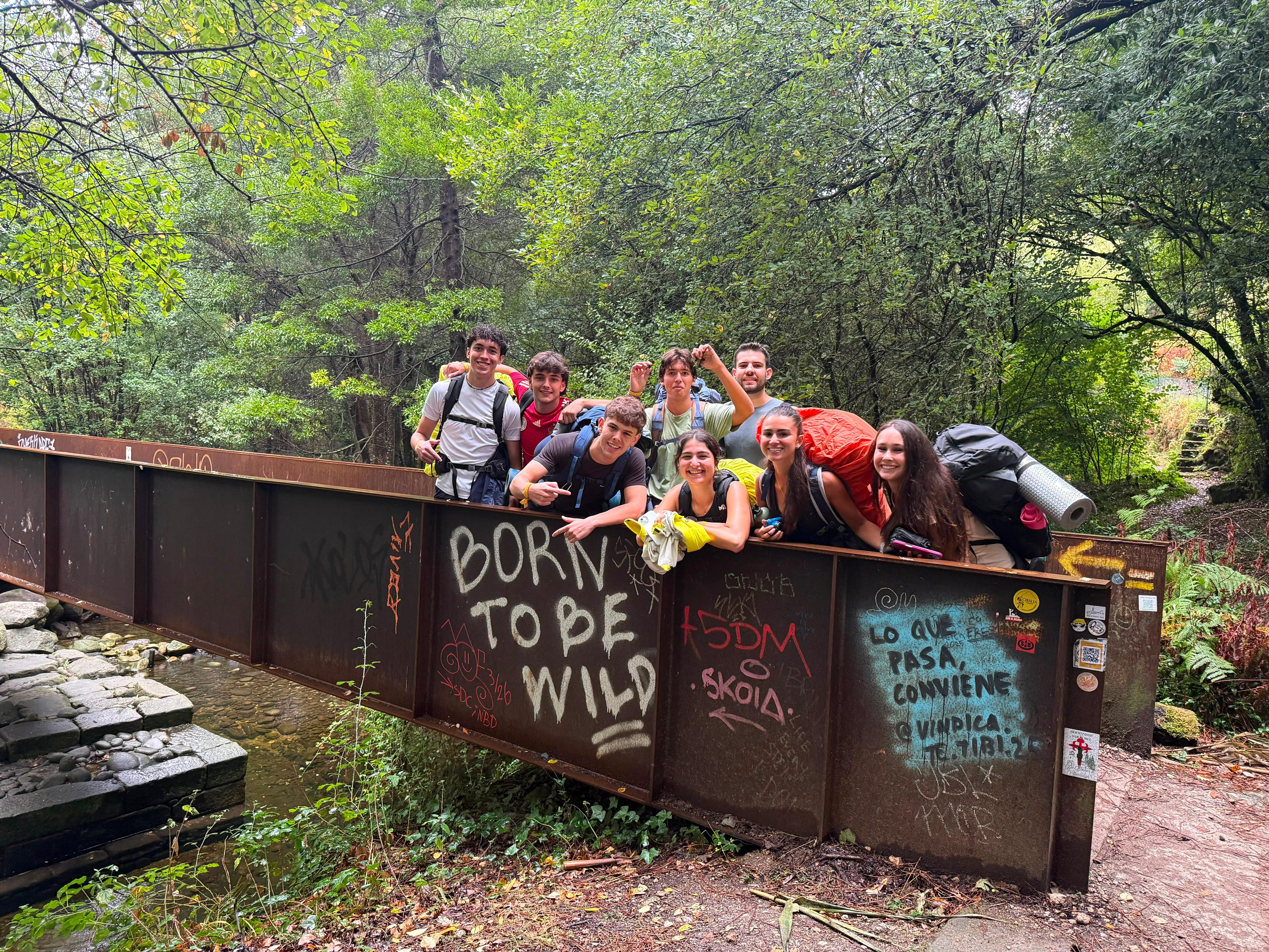 Un grupo de jóvenes posa felices en un puente rodeado de naturaleza.