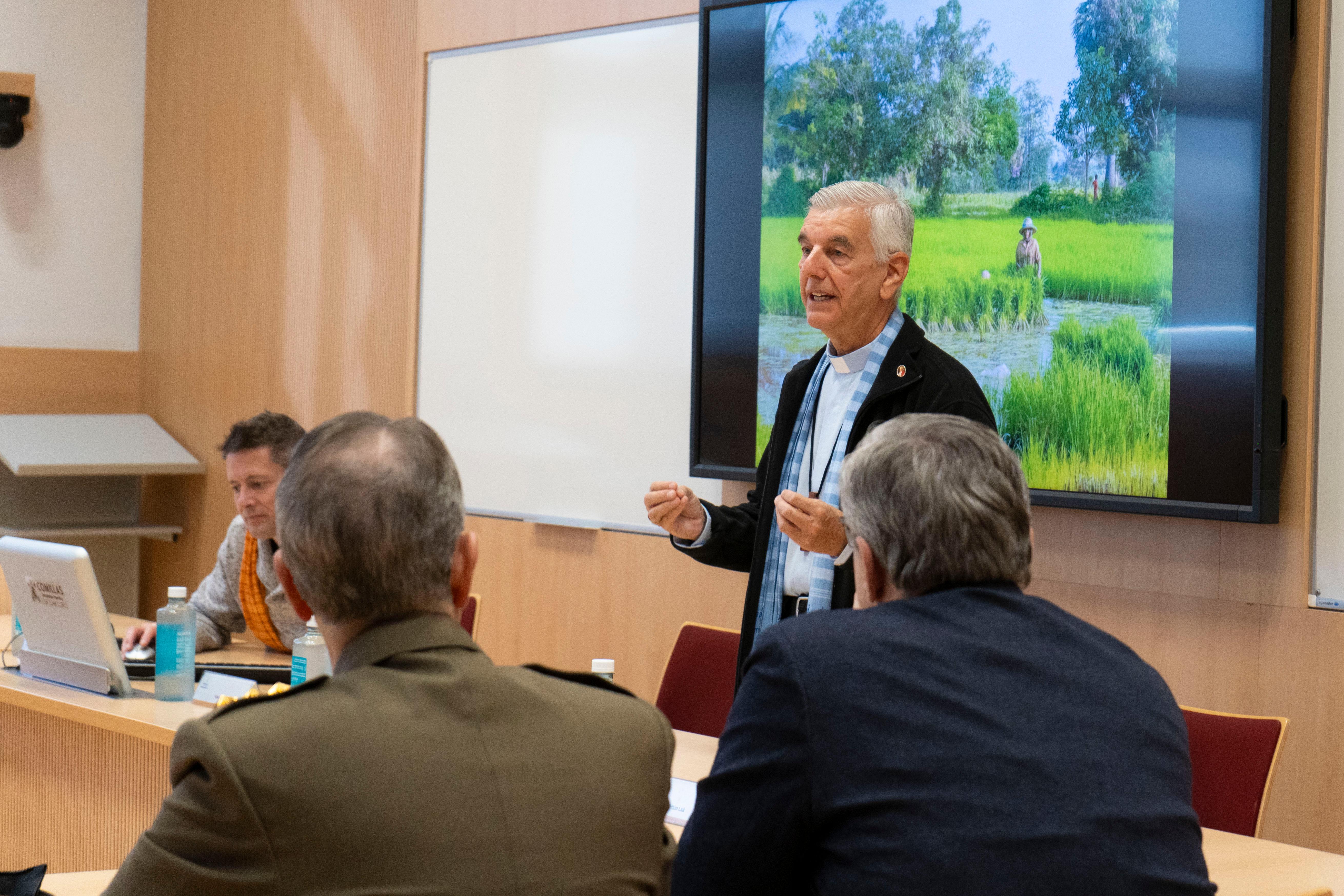 A man is presenting in a conference room with an image of a rural landscape projected behind him.