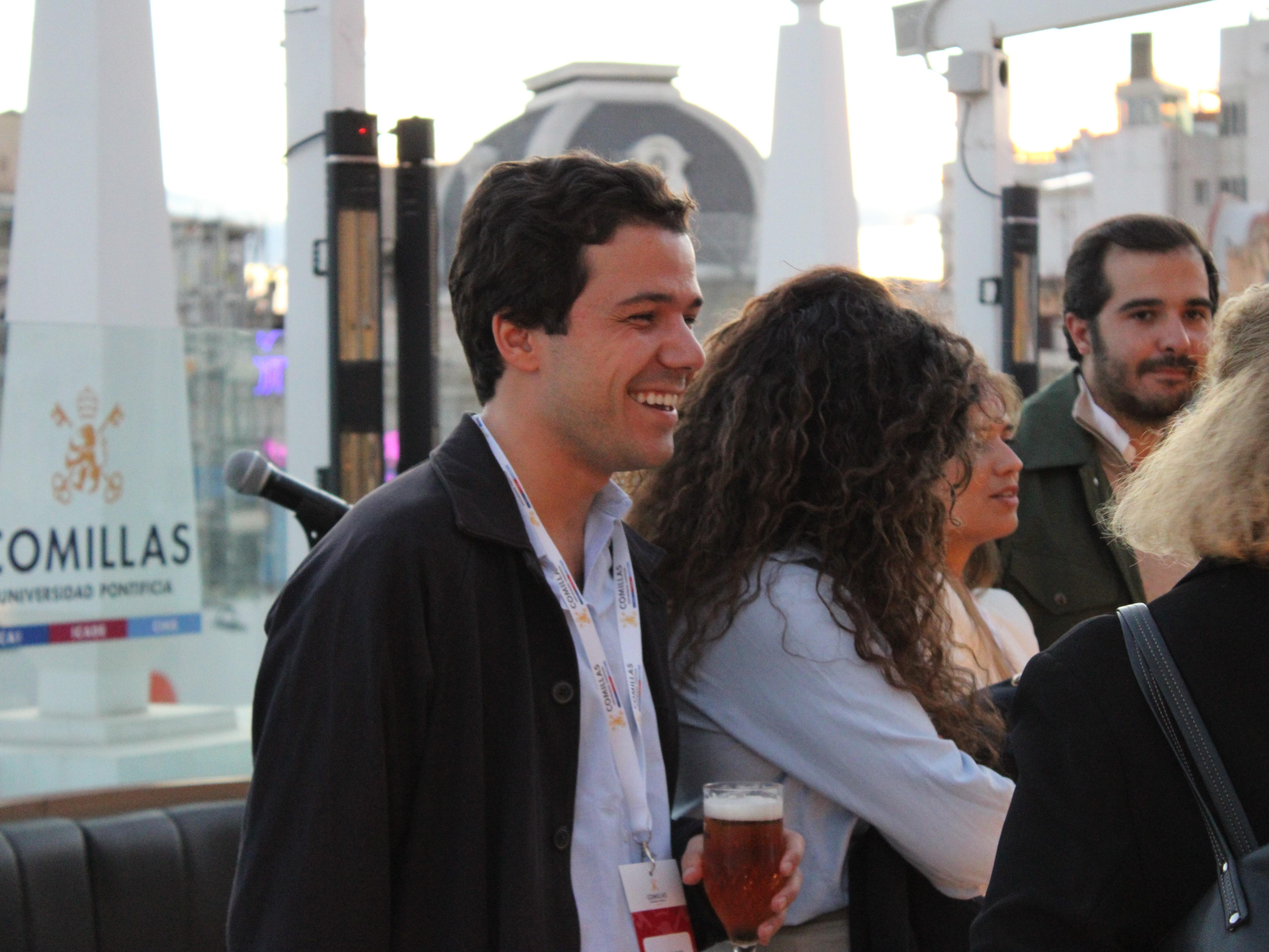 A man smiling at an outdoor social event with other people around, holding a beer.