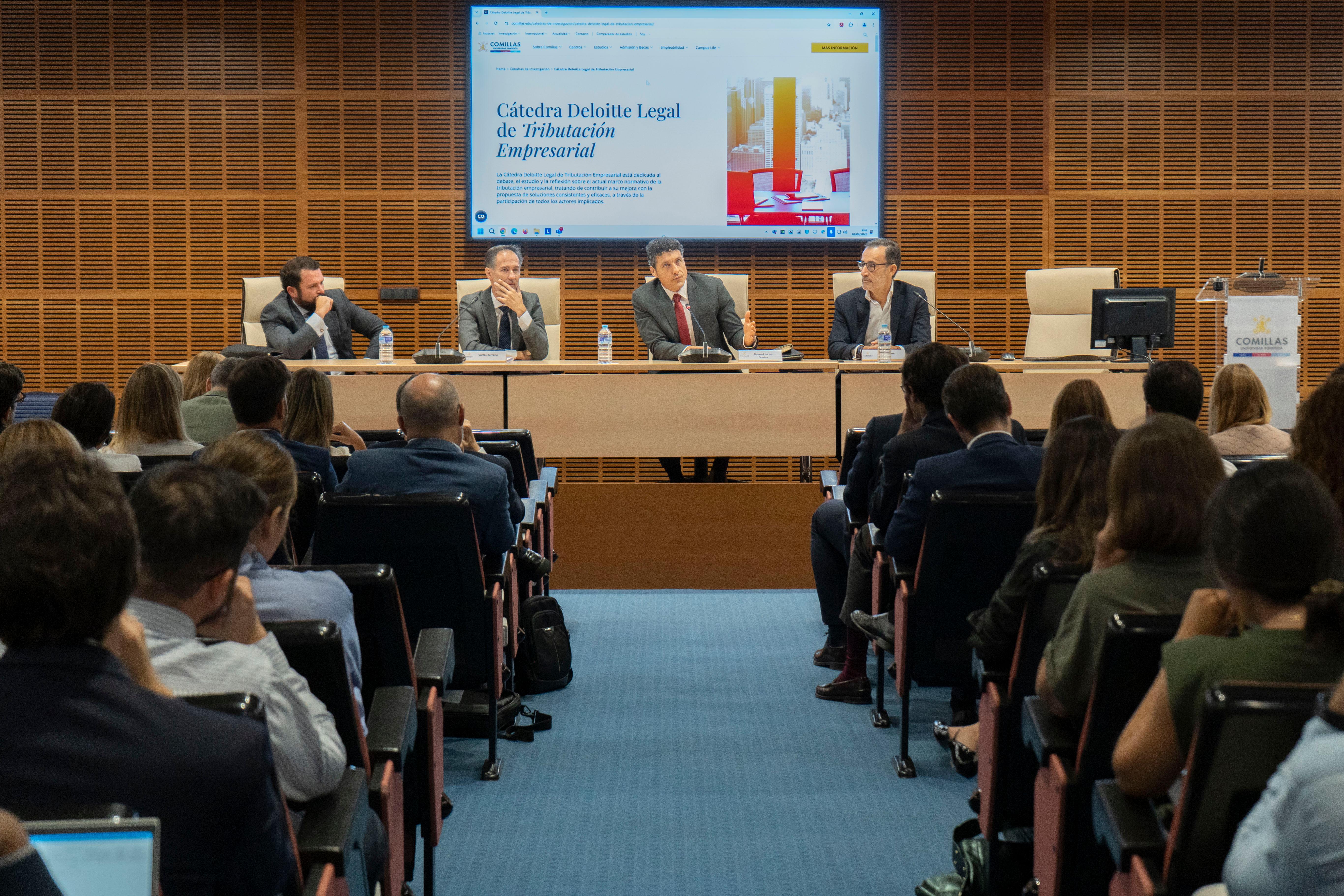 Un evento académico con varios ponentes en una mesa y una audiencia atenta.