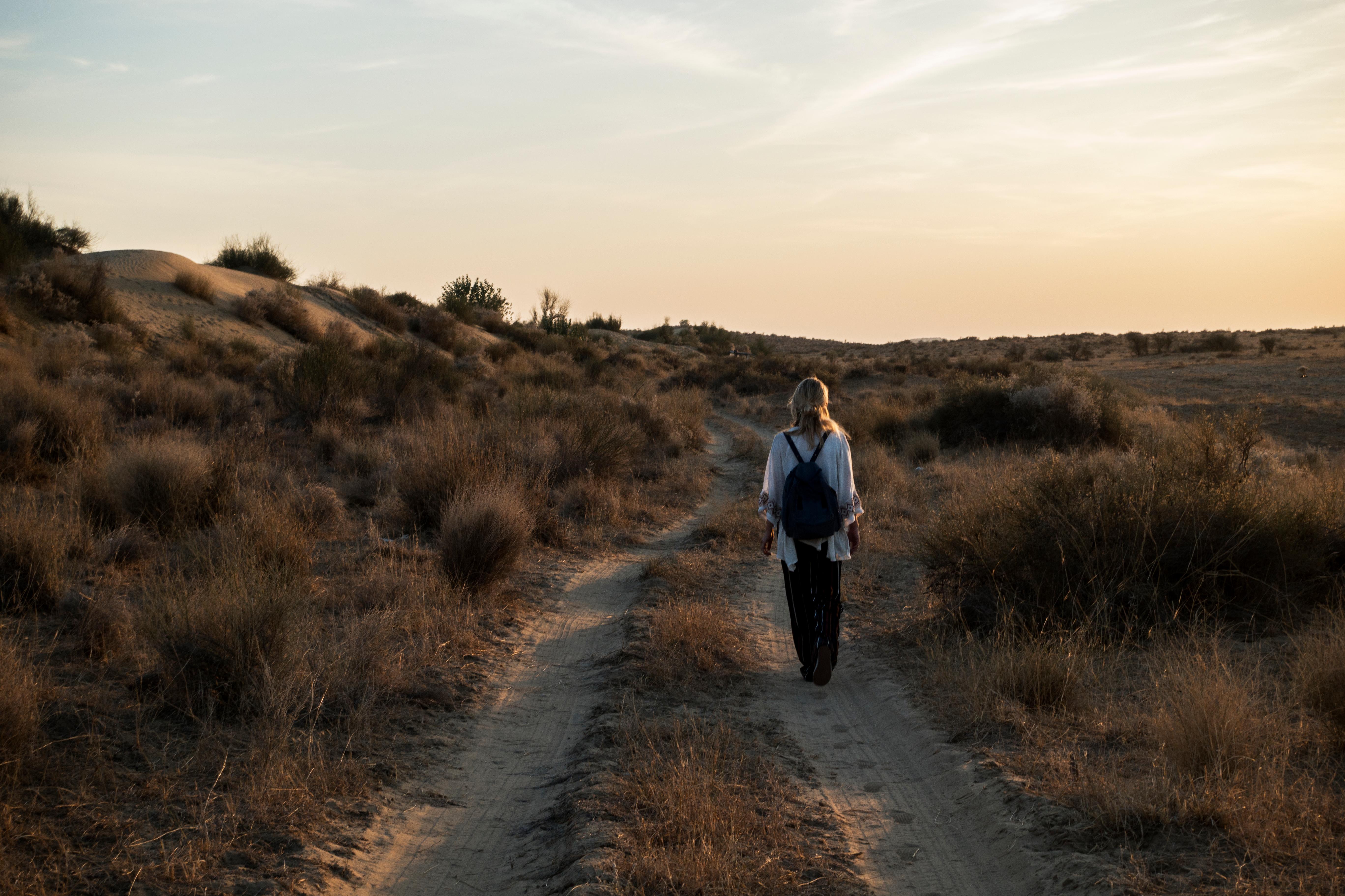 Una persona camina por un sendero en un paisaje desértico durante el atardecer.