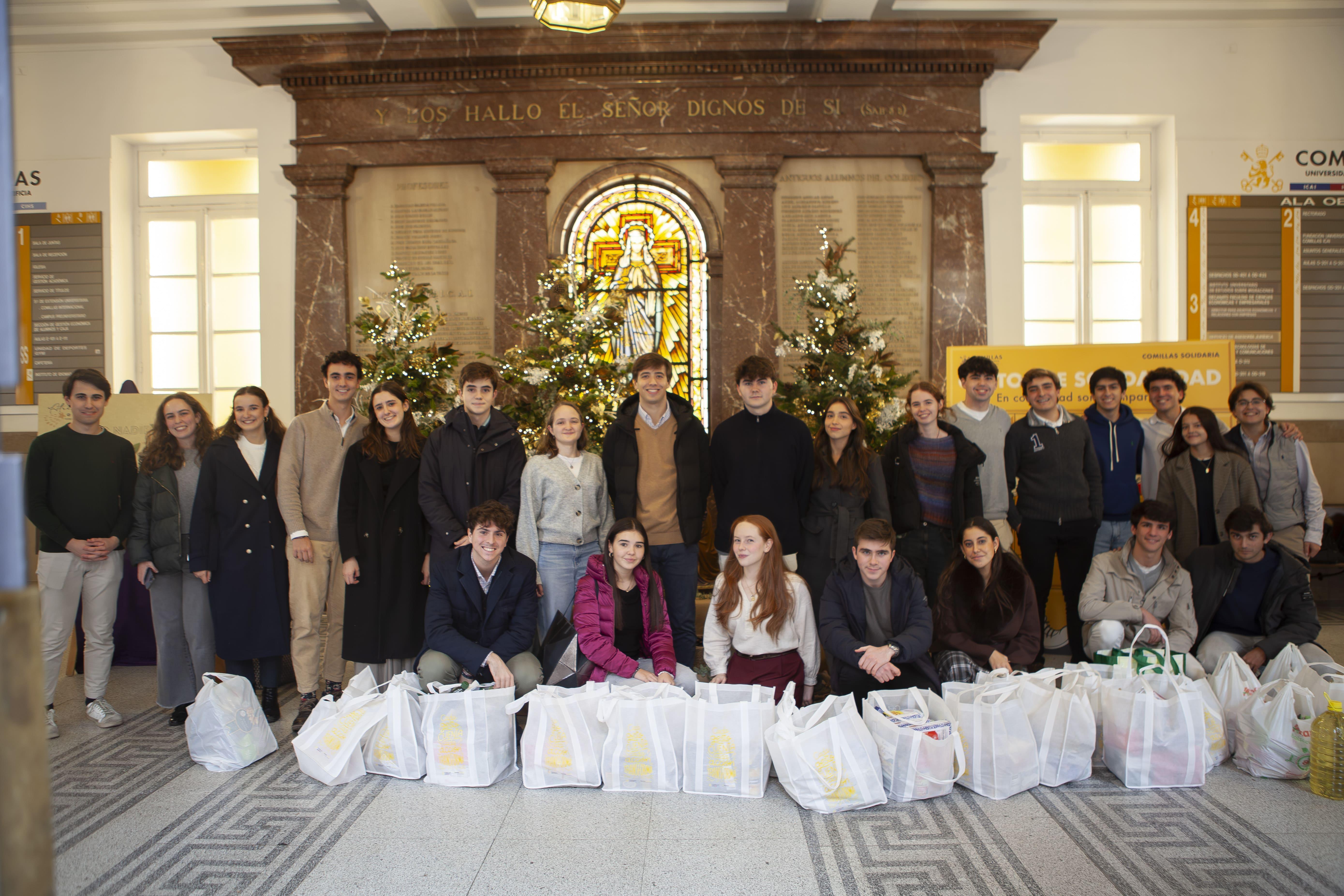 Grupo de personas posando frente a un altar decorado con árboles de Navidad y bolsas de regalo a sus pies.