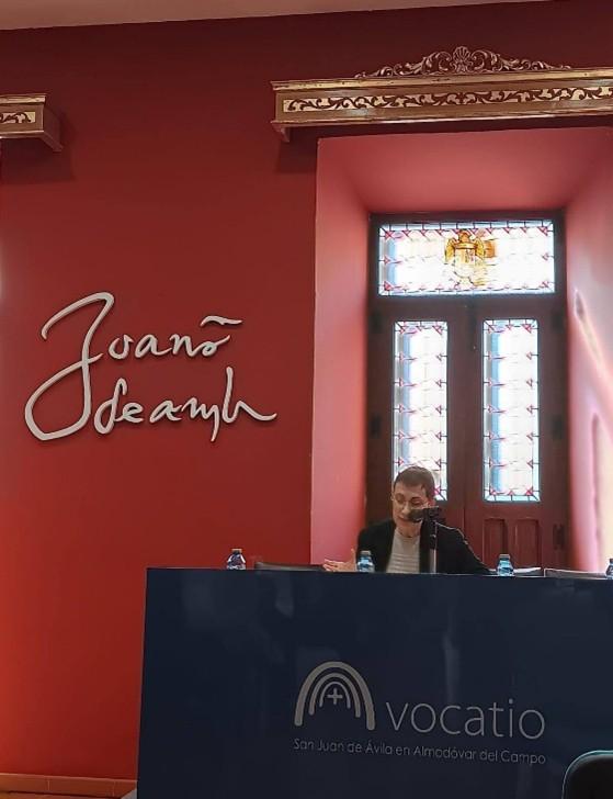 Una mujer sentada detrás de un escritorio en una sala con paredes rojas y una ventana con vidrieras coloridas.