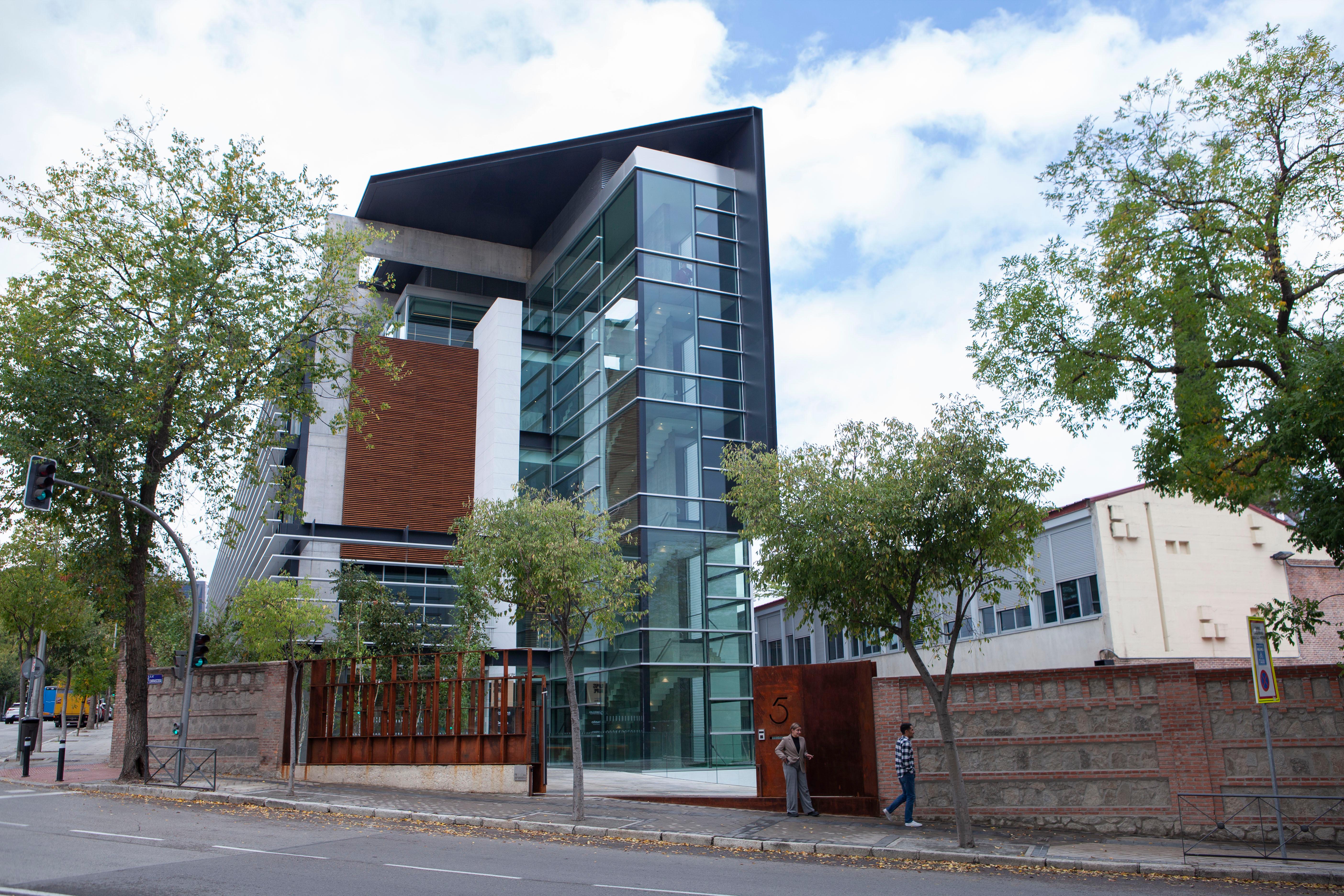 Edificio moderno con grandes ventanales y varios niveles, rodeado de árboles.