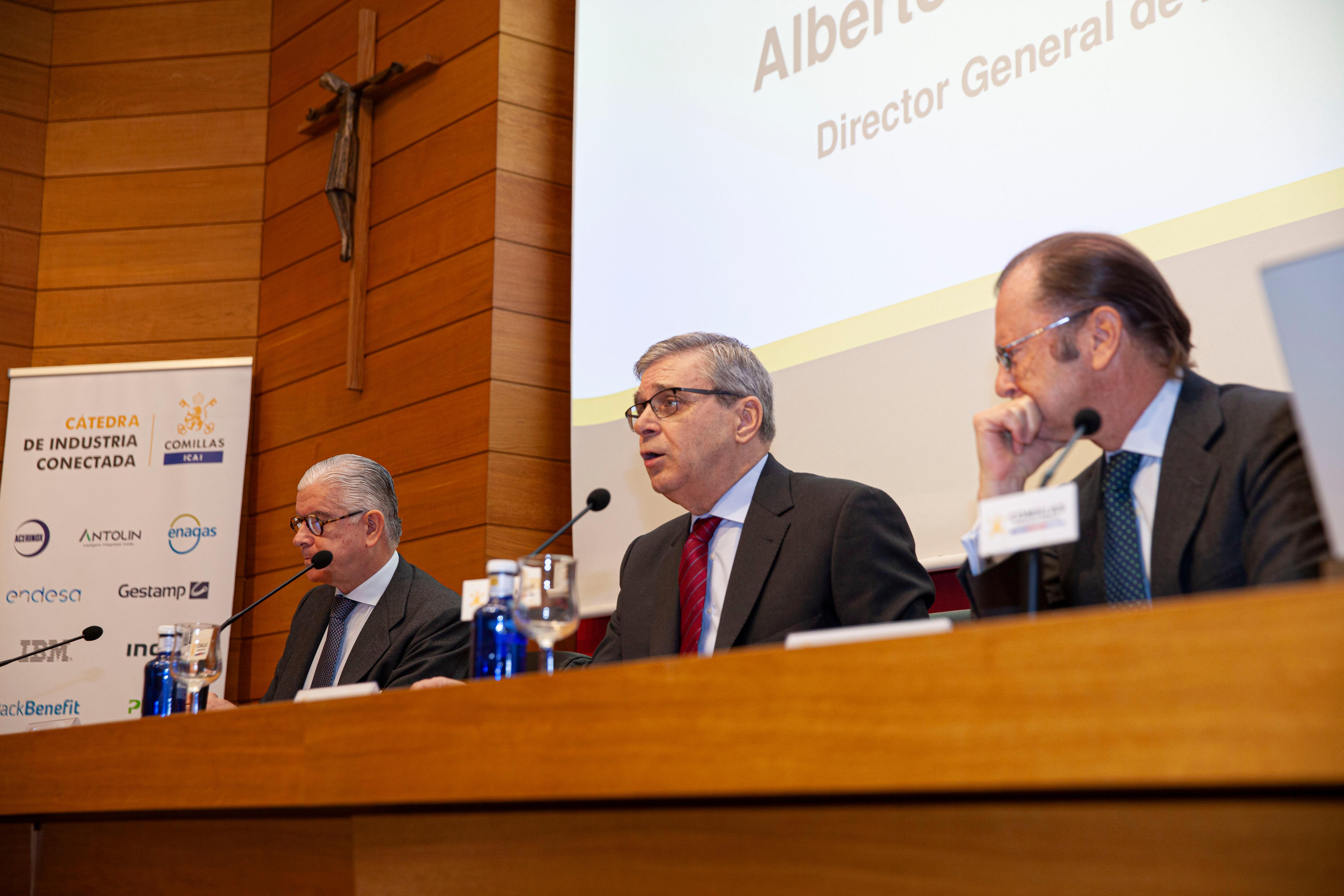 Tres hombres de mediana edad vestidos con traje y corbata están sentados frente a micrófonos en un panel de conferencias.