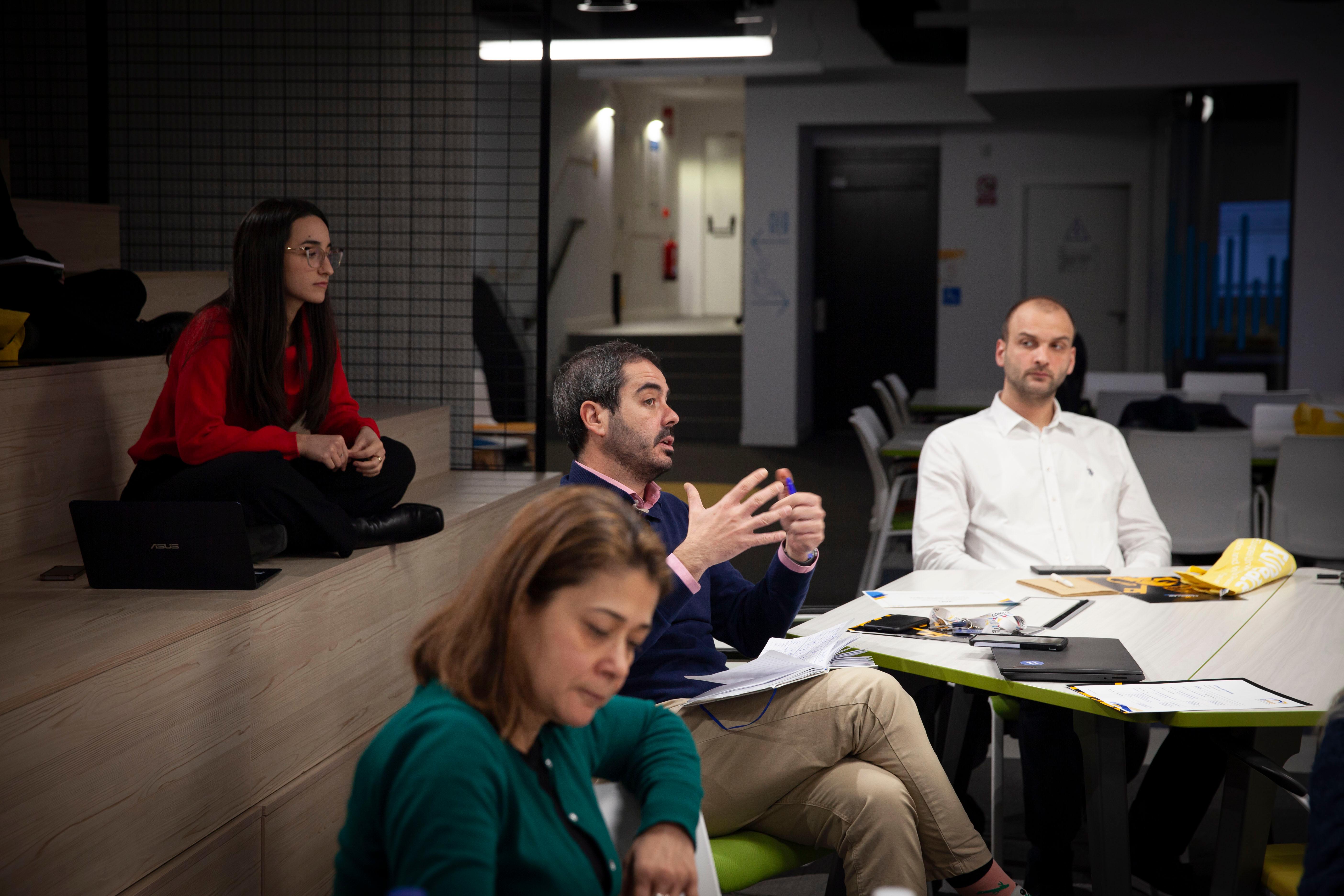 Personas sentadas en una oficina moderna, escuchando atentamente a un hombre que está hablando y gesticulando.