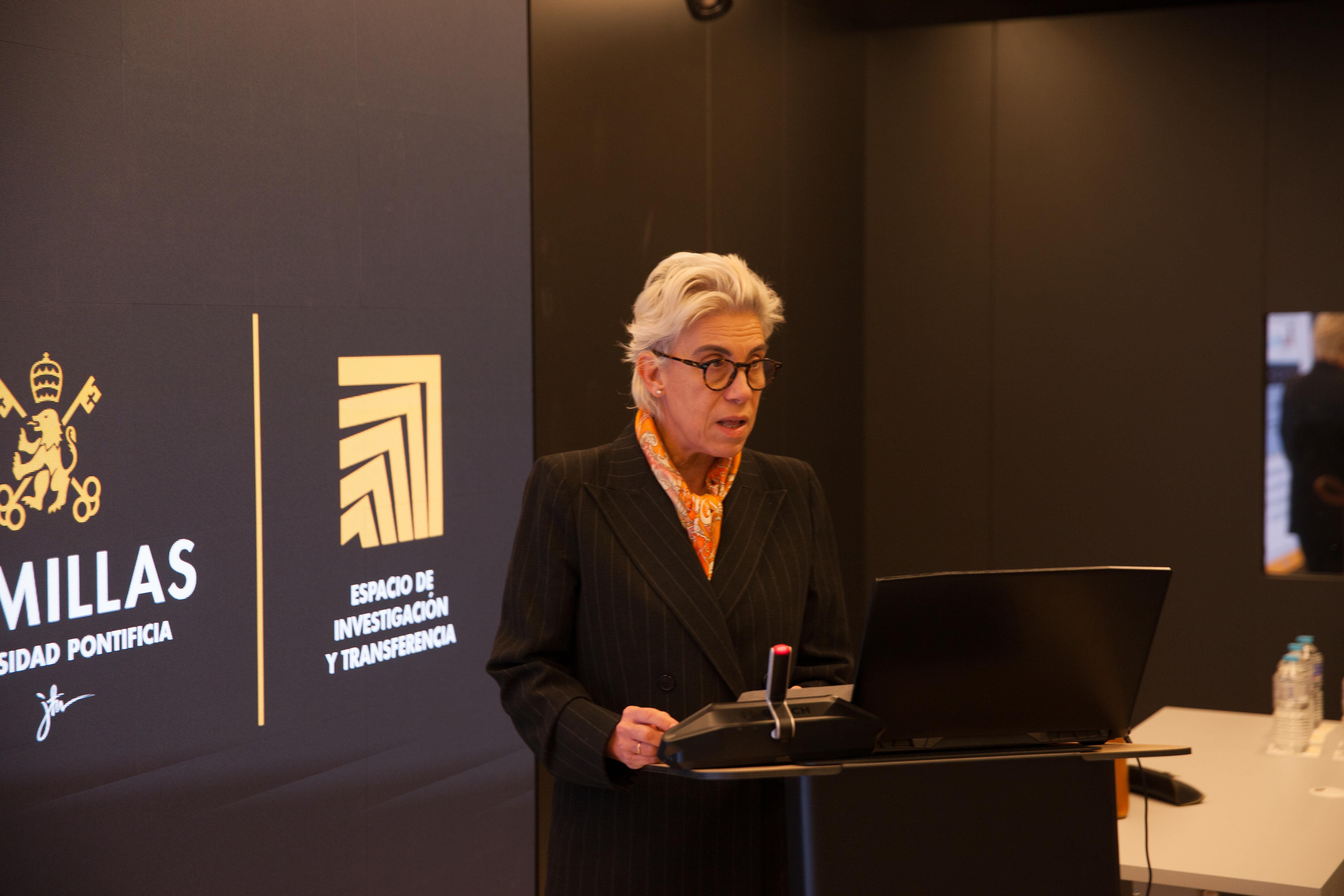 Una mujer con cabello canoso está hablando frente a un podio en un evento formal.
