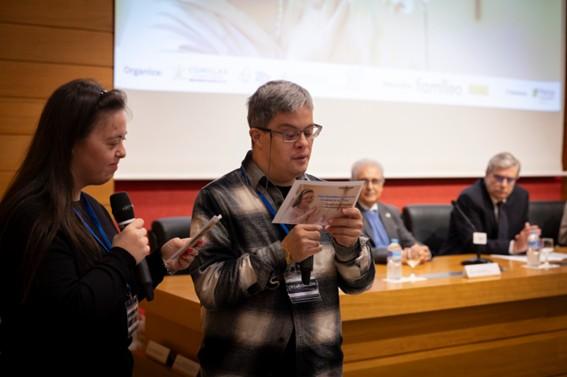 Una presentación en un evento donde dos personas comparten información frente a un público en una mesa de conferencias.