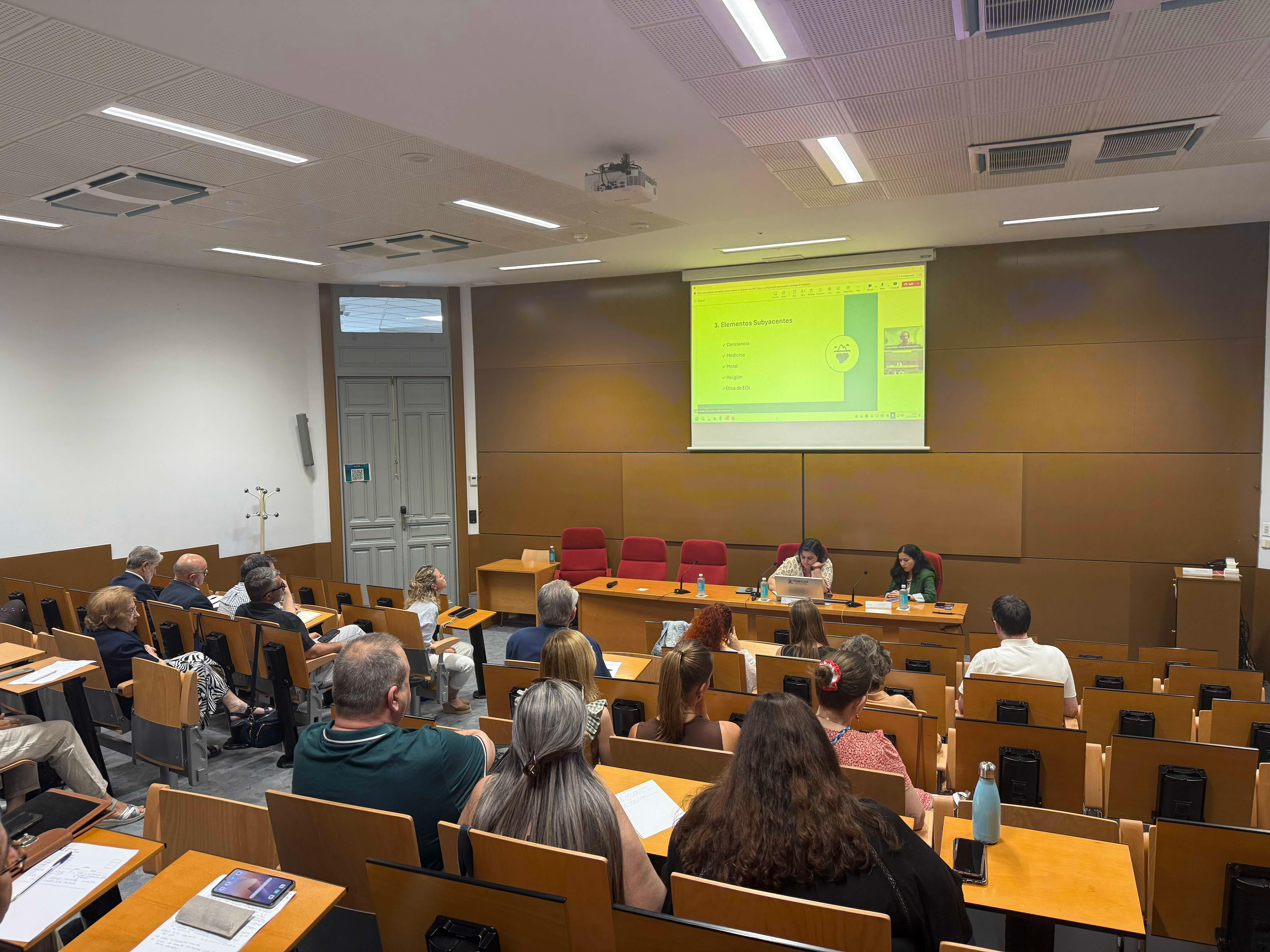 Una sala de conferencias con público prestando atención a un presentador que está hablando frente a una pantalla.