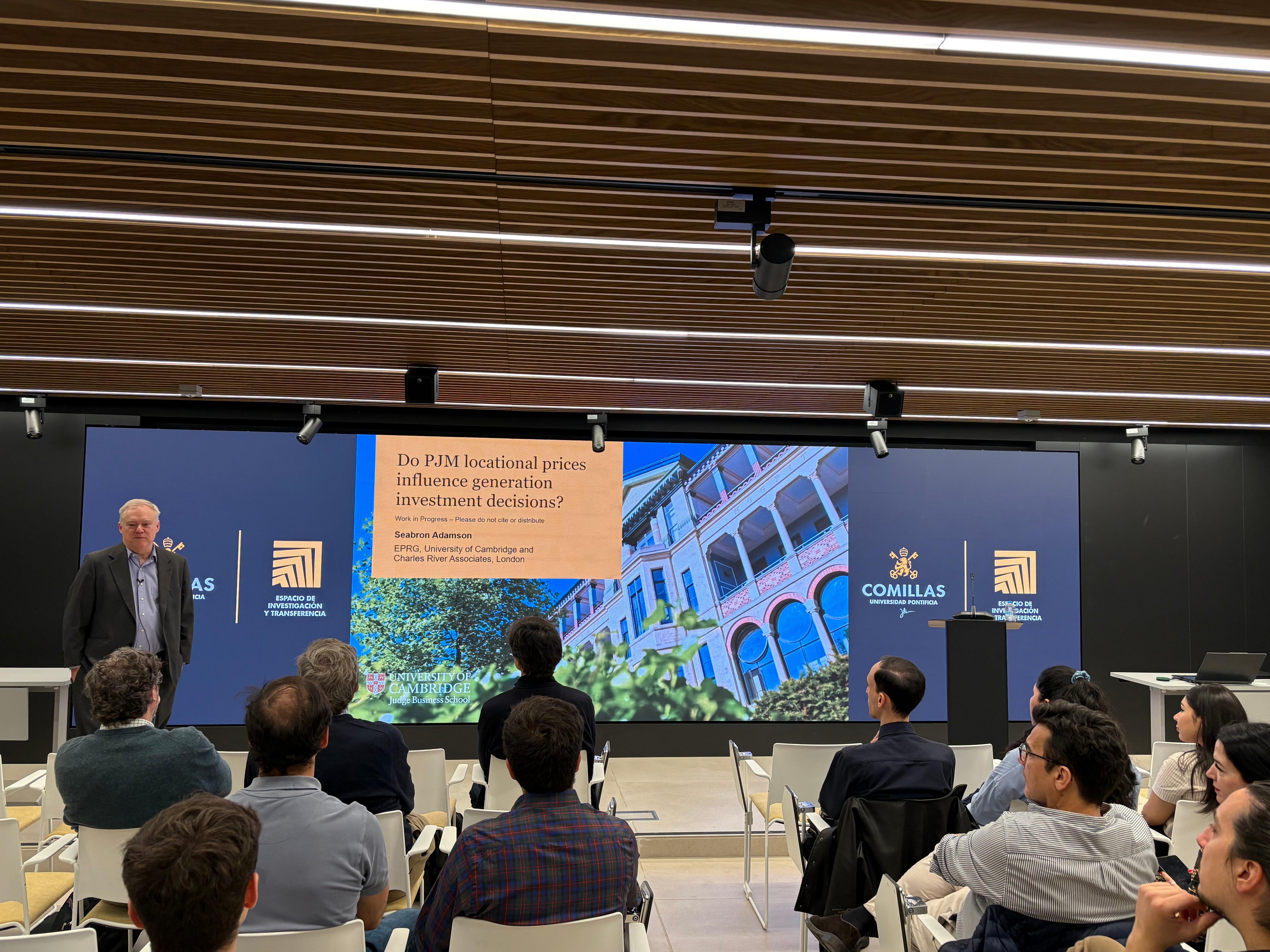 Un ponente presenta un tema sobre precios de localización en un auditorio moderno lleno de personas.