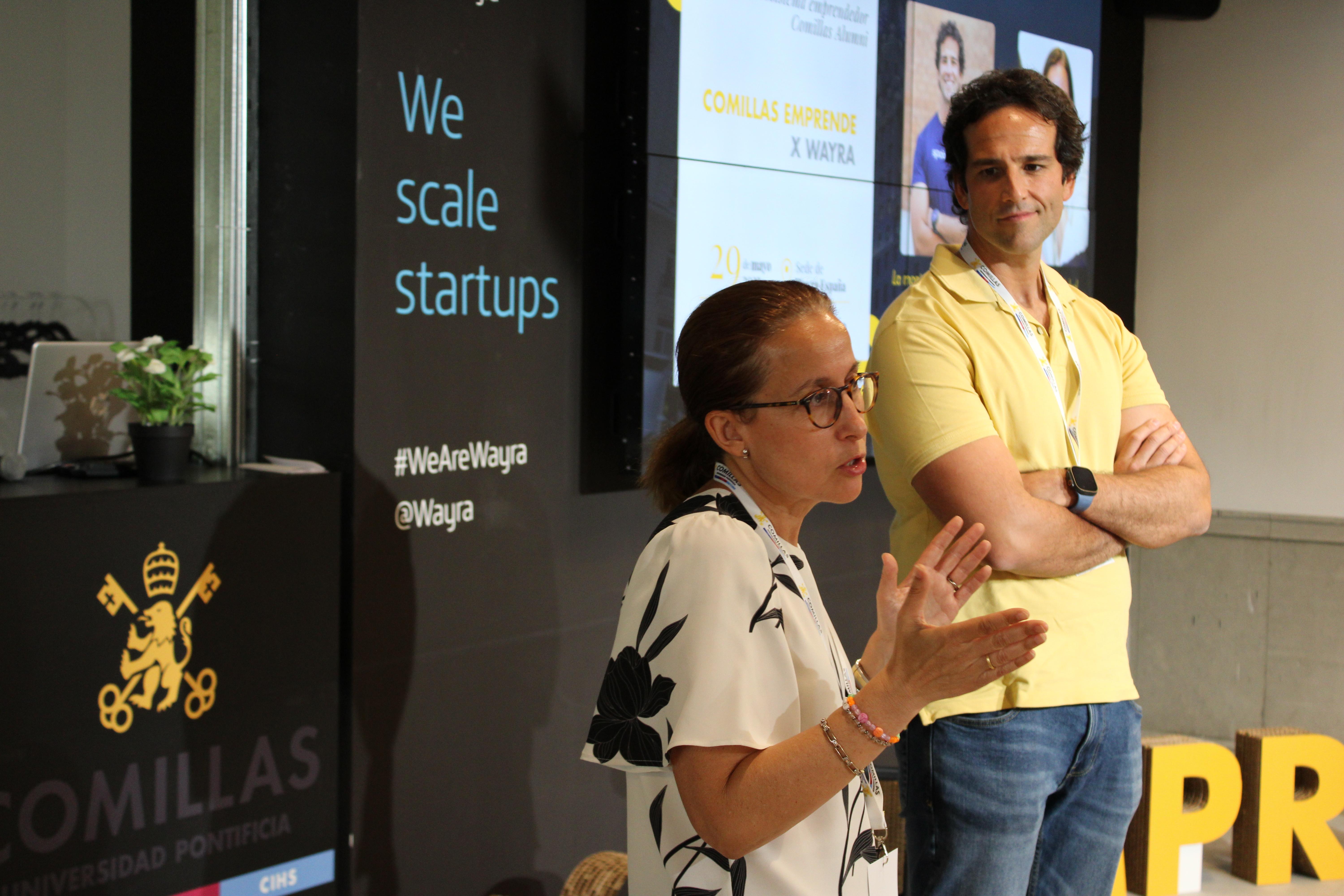 Una mujer habla frente a un público mientras un hombre observa en un evento de startups.