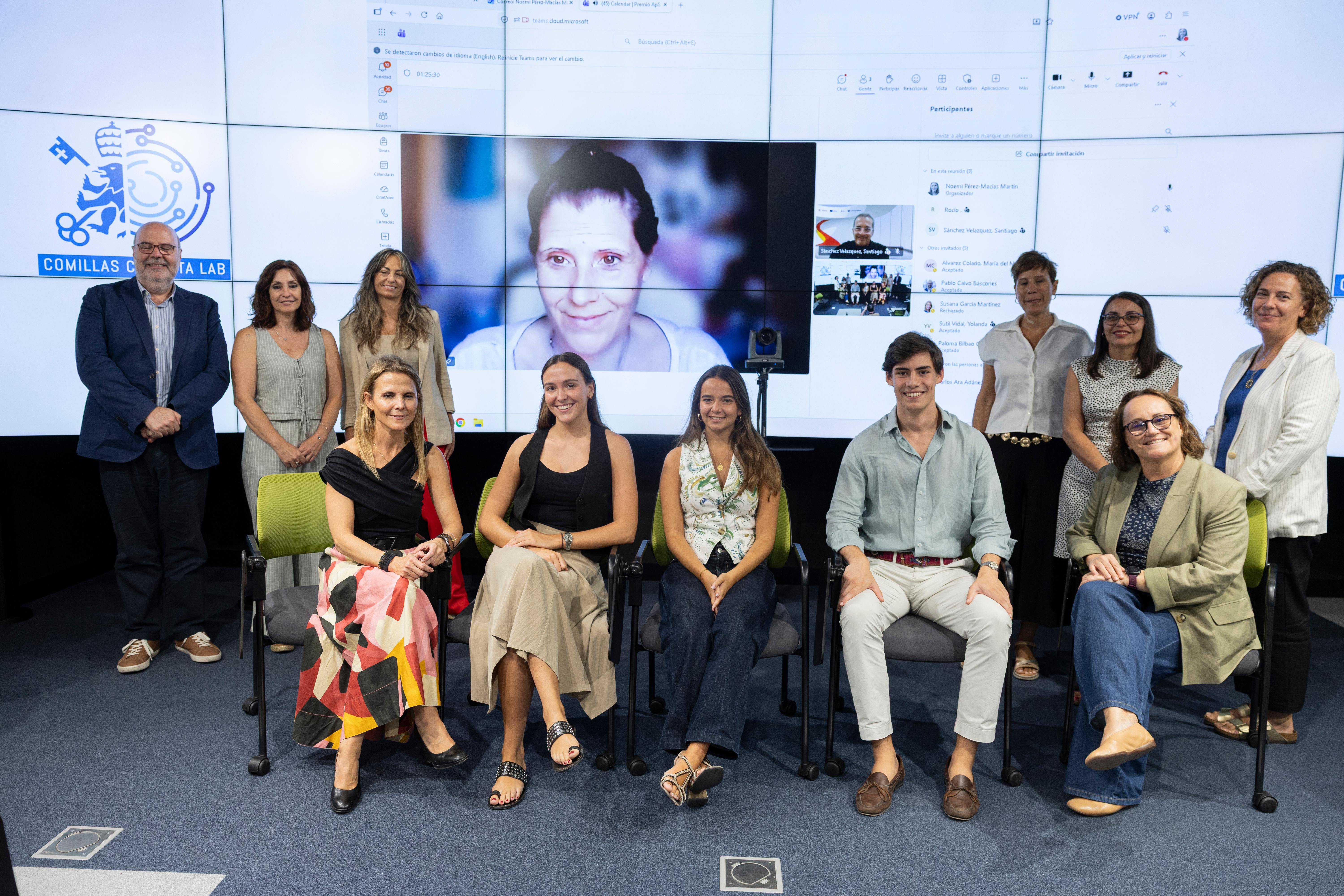 Grupo de personas posando frente a una pantalla, con una mujer en videollamada en el centro.