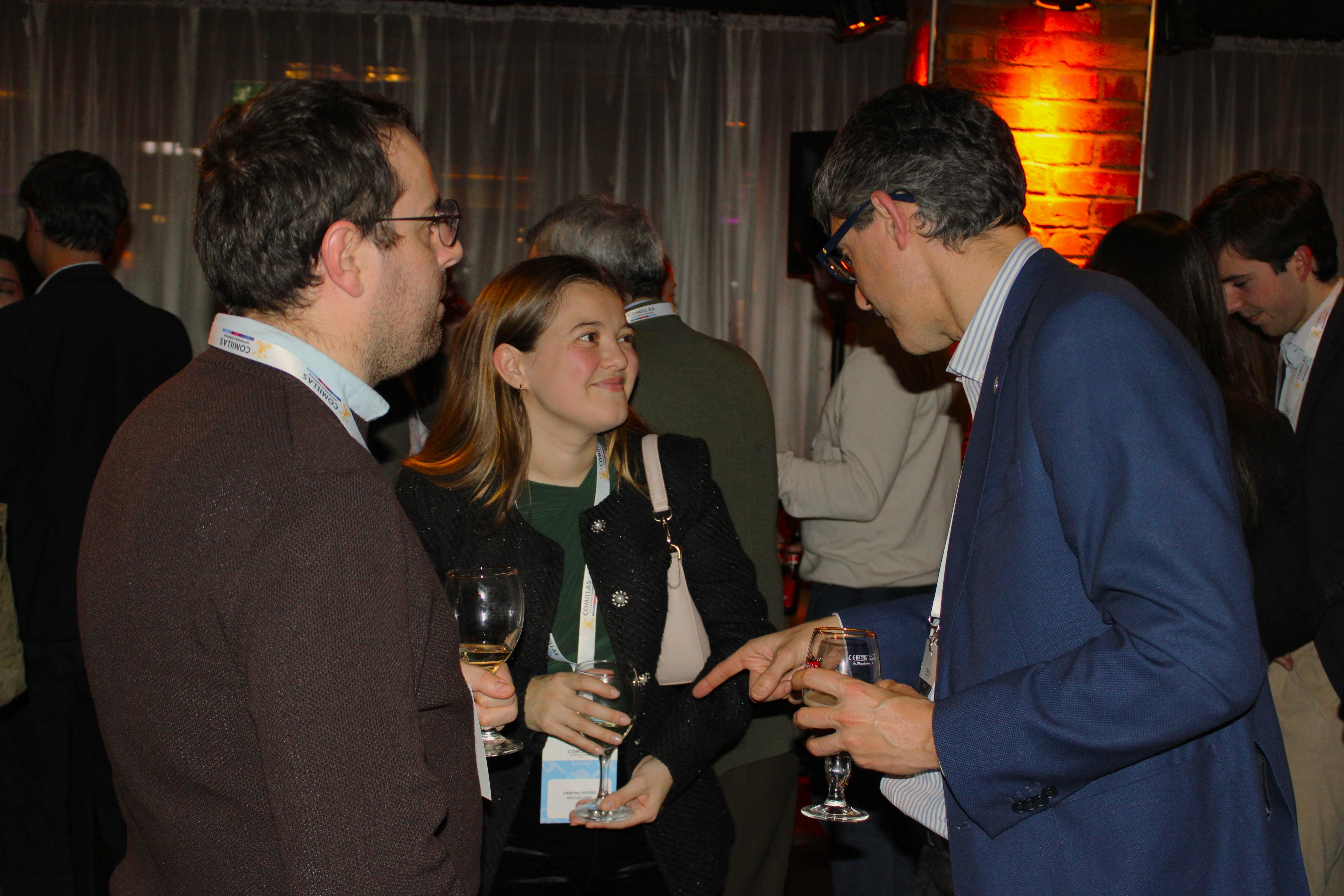 Tres personas conversando en un evento social con copas de vino en sus manos.