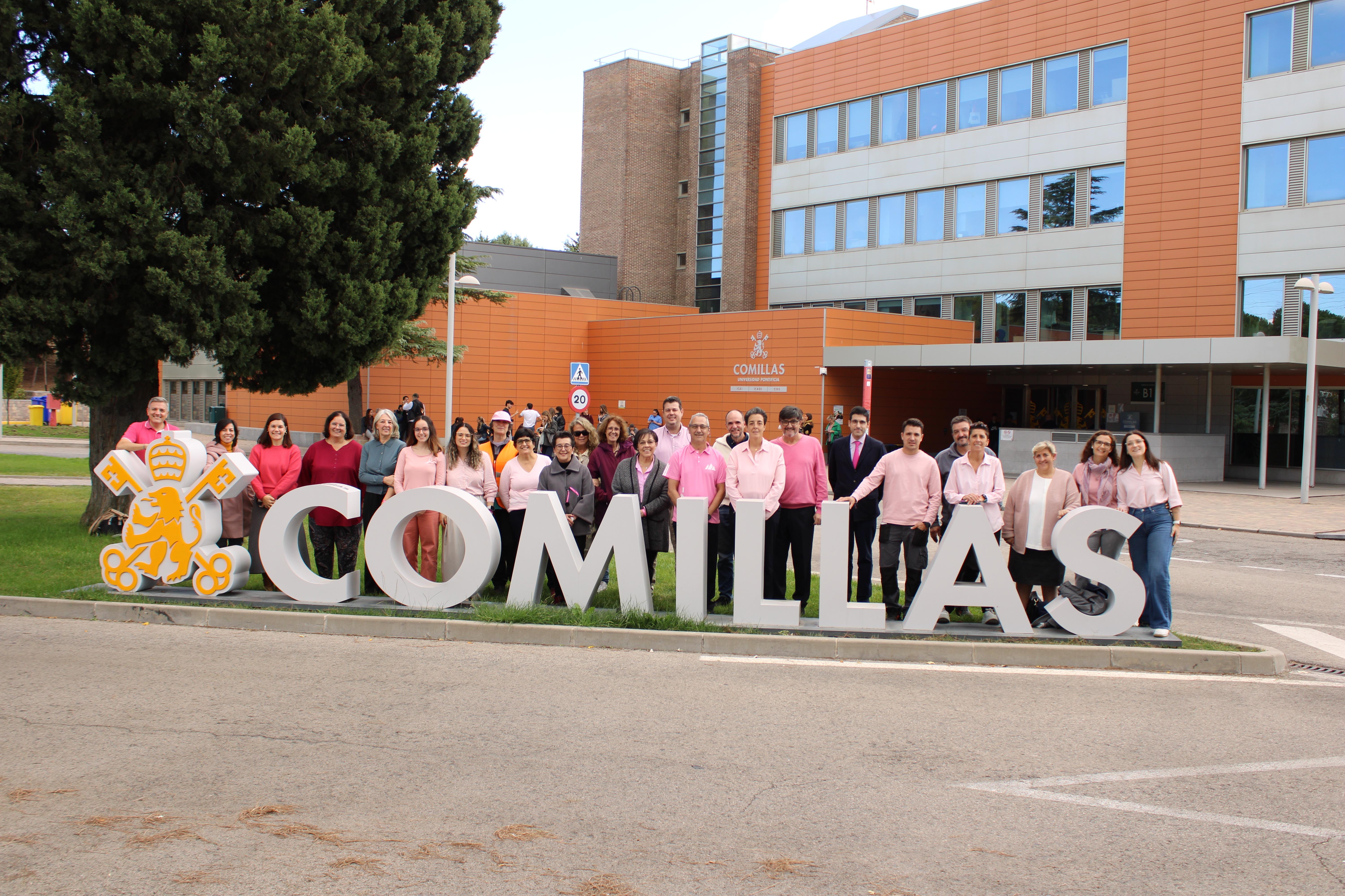 Un grupo de personas vestidas de rosa posando frente al cartel de la Universidad Pontificia Comillas.