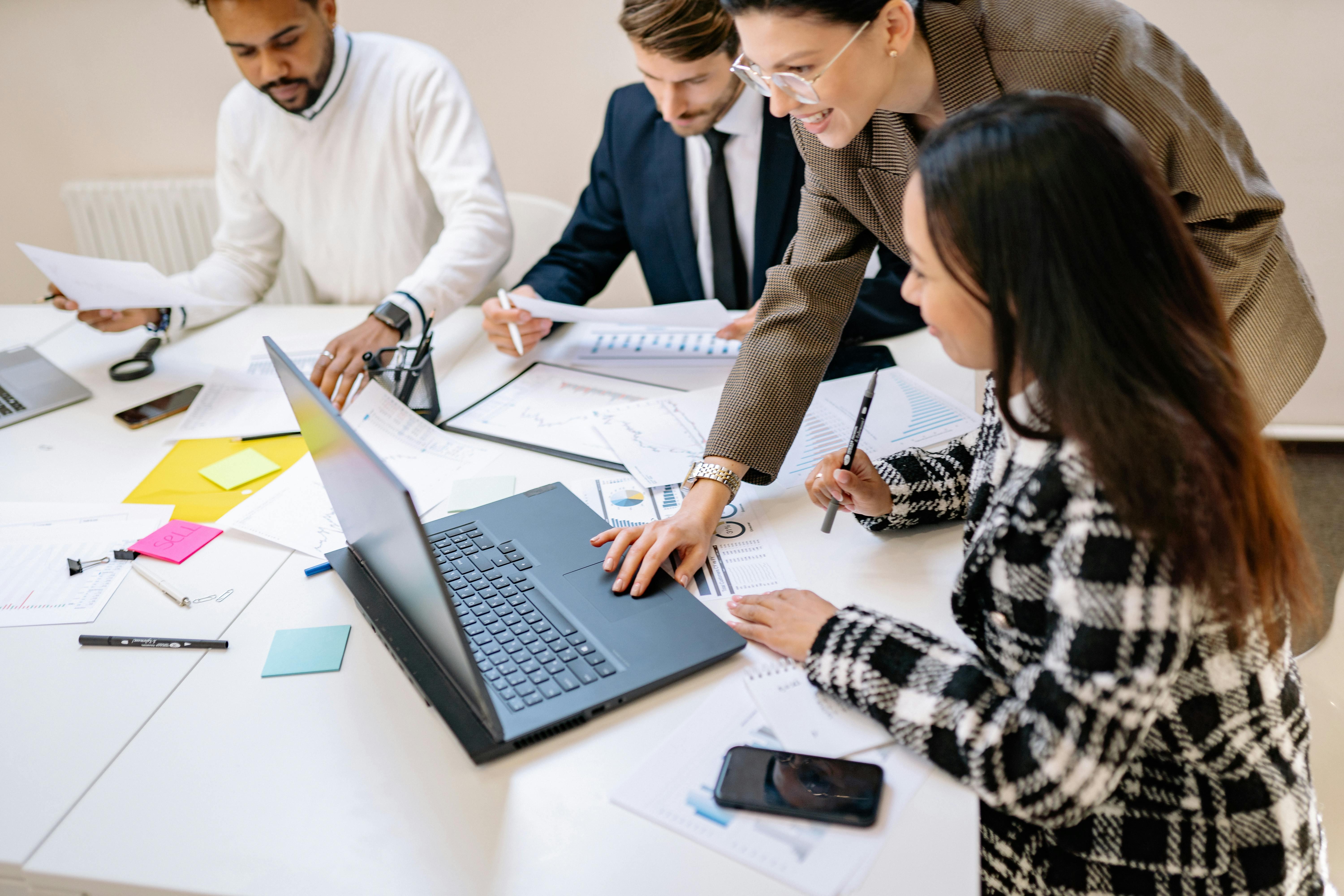 Un grupo de profesionales trabaja colaborativamente alrededor de una mesa, utilizando una computadora portátil y documentos.