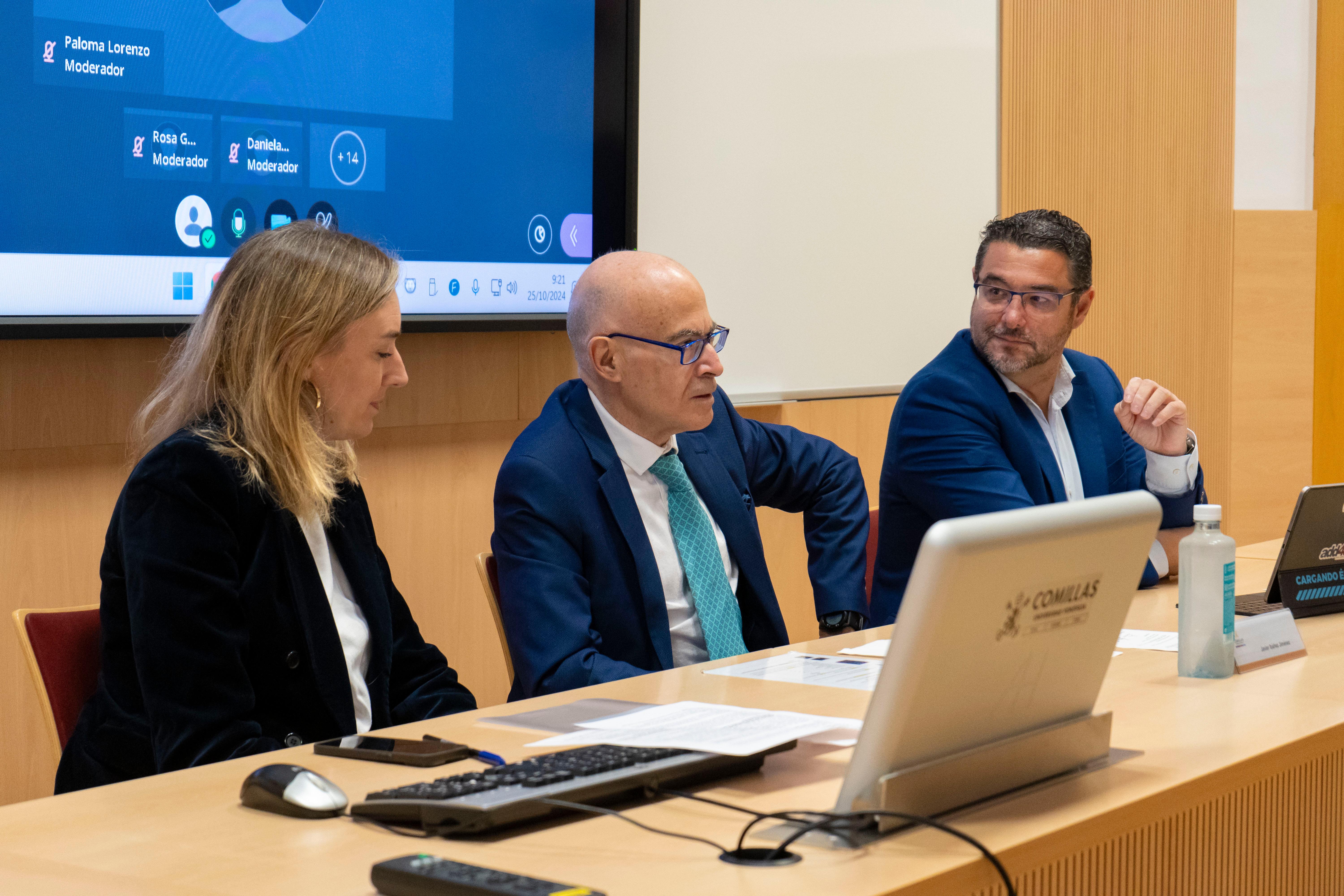 Three professionals, two men and a woman, are seated at a table during a business meeting with a laptop in front of them.