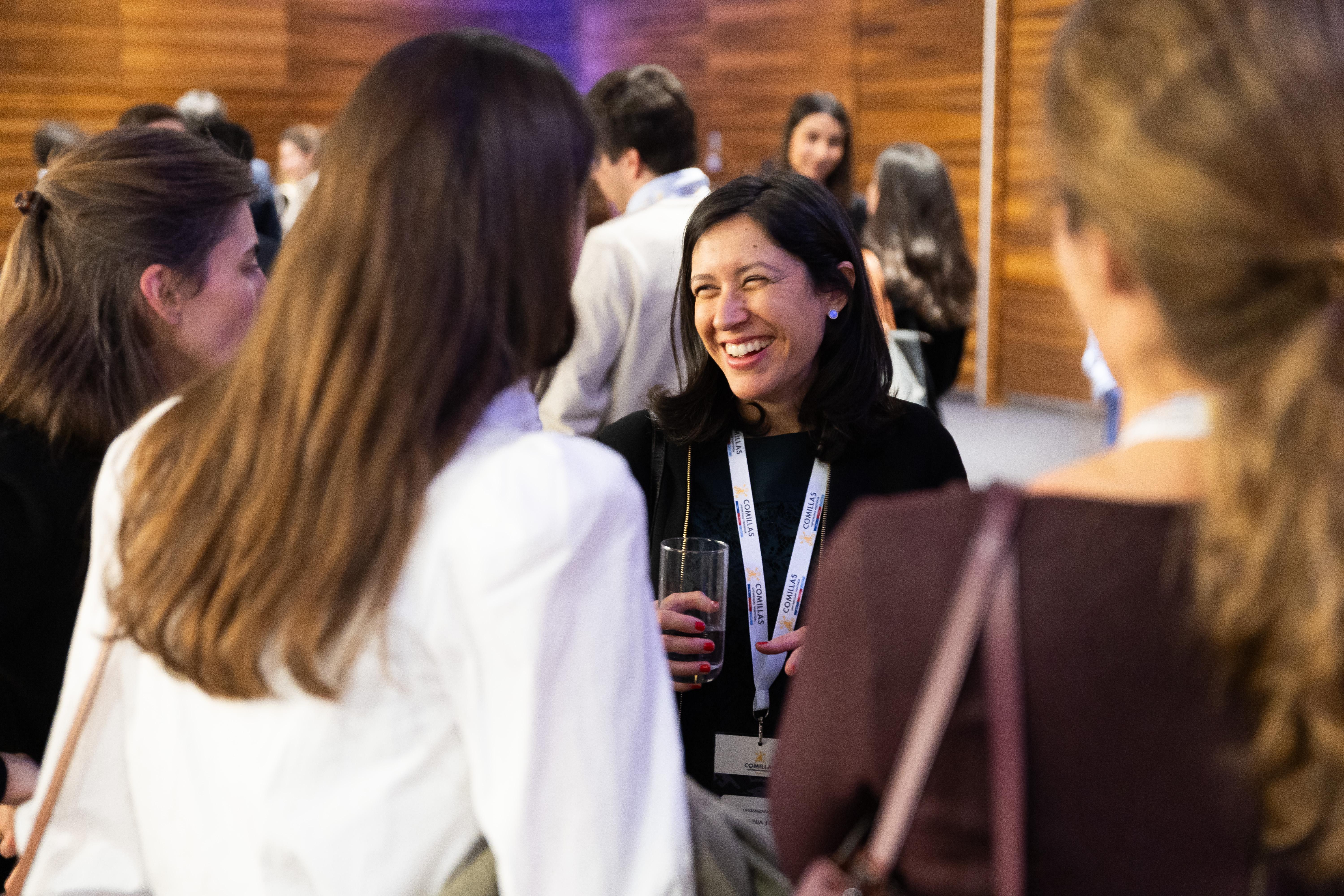 Un grupo de personas conversando en un evento social, con una mujer sonriente en el centro de la imagen.