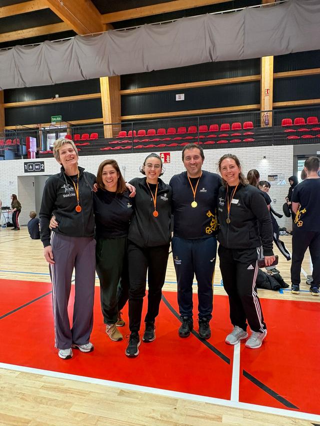 Un grupo de cinco personas sonríen y posan con medallas en un ambiente deportivo.