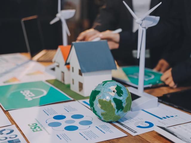 Una mesa de trabajo muestra maquetas de casas y turbinas eólicas junto a gráficos relacionados con la sostenibilidad.