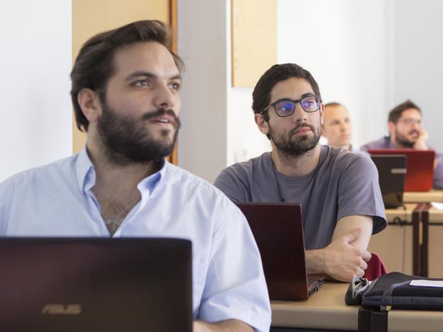 Estudiantes en aula universitaria con ordenadores portátiles, participando en clase en la Universidad de Comillas.
