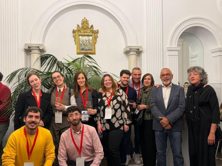 Un grupo de personas posando en un evento, con decoraciones elegantes y plantas de fondo.