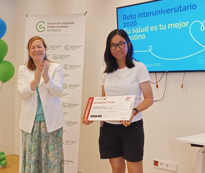 Una mujer sonriente sostiene un certificado mientras otra mujer aplaude en un evento.