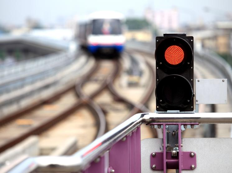A red traffic signal light in focus with a blurred train approaching on railway tracks in the background.