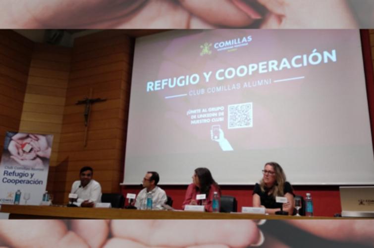 A panel of four people sitting on a stage with a presentation titled 'REFUGIO Y COOPERACIÓN' displayed on a large screen behind them.
