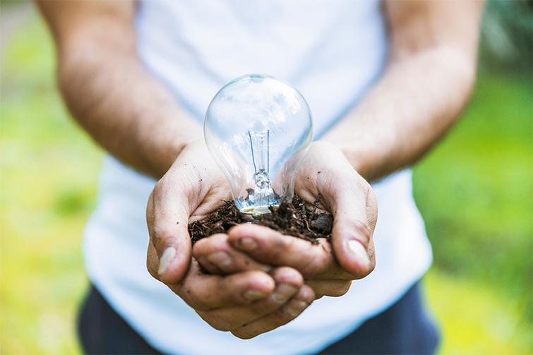 A person holding a light bulb with soil in their hands, symbolizing eco-friendly energy concepts.