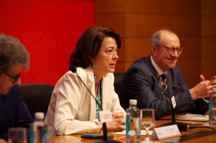 A woman and two men participating in a panel discussion at a conference, seated at a table with microphones and water bottles.