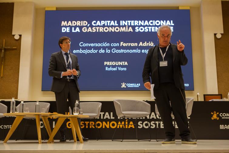 Two men are standing on a stage; one is speaking and the other listening, in front of a backdrop about Madrid being the international capital of sustainable gastronomy.