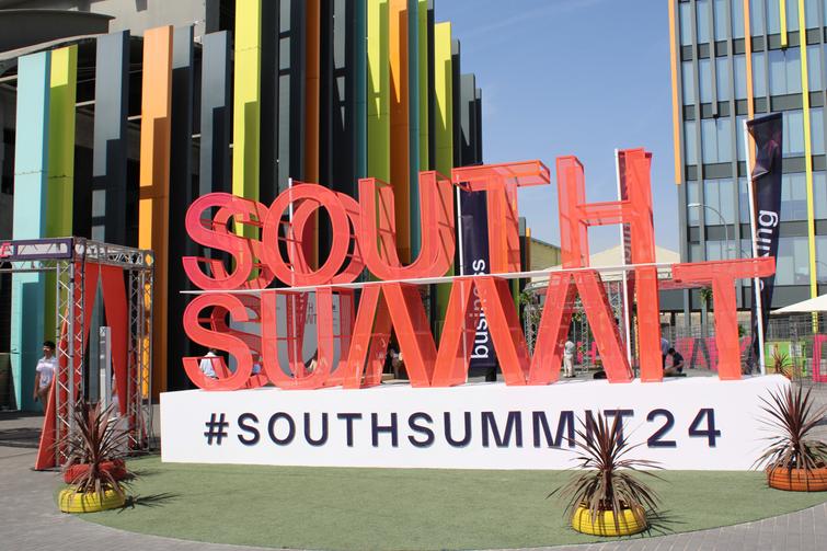A colorful large sign reading 'SOUTH SUMMIT' in front of a modern building with vibrant architectural elements.